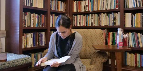 A student sits in a library room reading surrounded by books