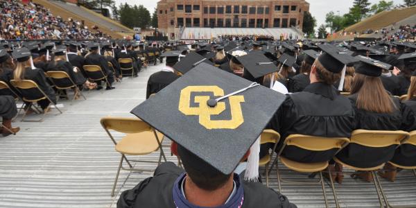 A student wearing a customized CU mortar board at a past campus graduation ceremony at Folsom Field
