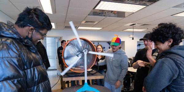 A wind team member in a propeller beanie demonstrates a tabletop turbine model during at K-12 outreach event