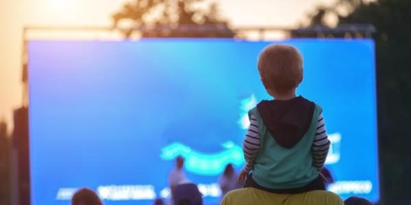 Child sitting on his father's neck watching a movie in the open air