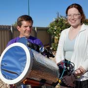 Man and woman stand behind a telescope on a sunny day